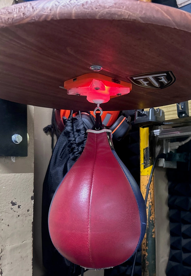 A red speed bag under the glowing orange counter on a wood platform in a garage