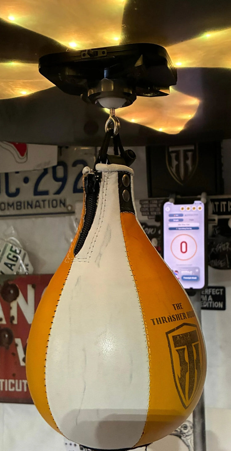 A yellow and white Thrasher speed bag under the counter in a garage hung with license plates, the app open on a phone